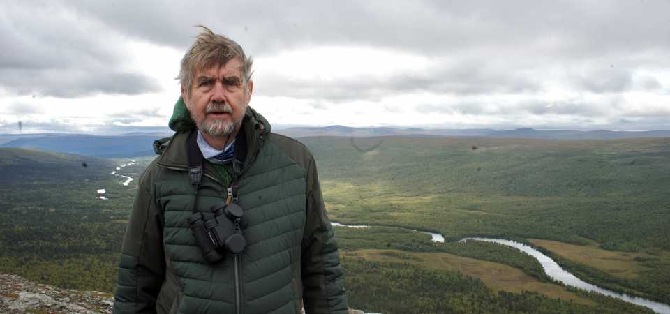 Dag Jonzon Dag Jonzon står med kikare om halsen med ett vackert bergslandskap i bakgrunden.